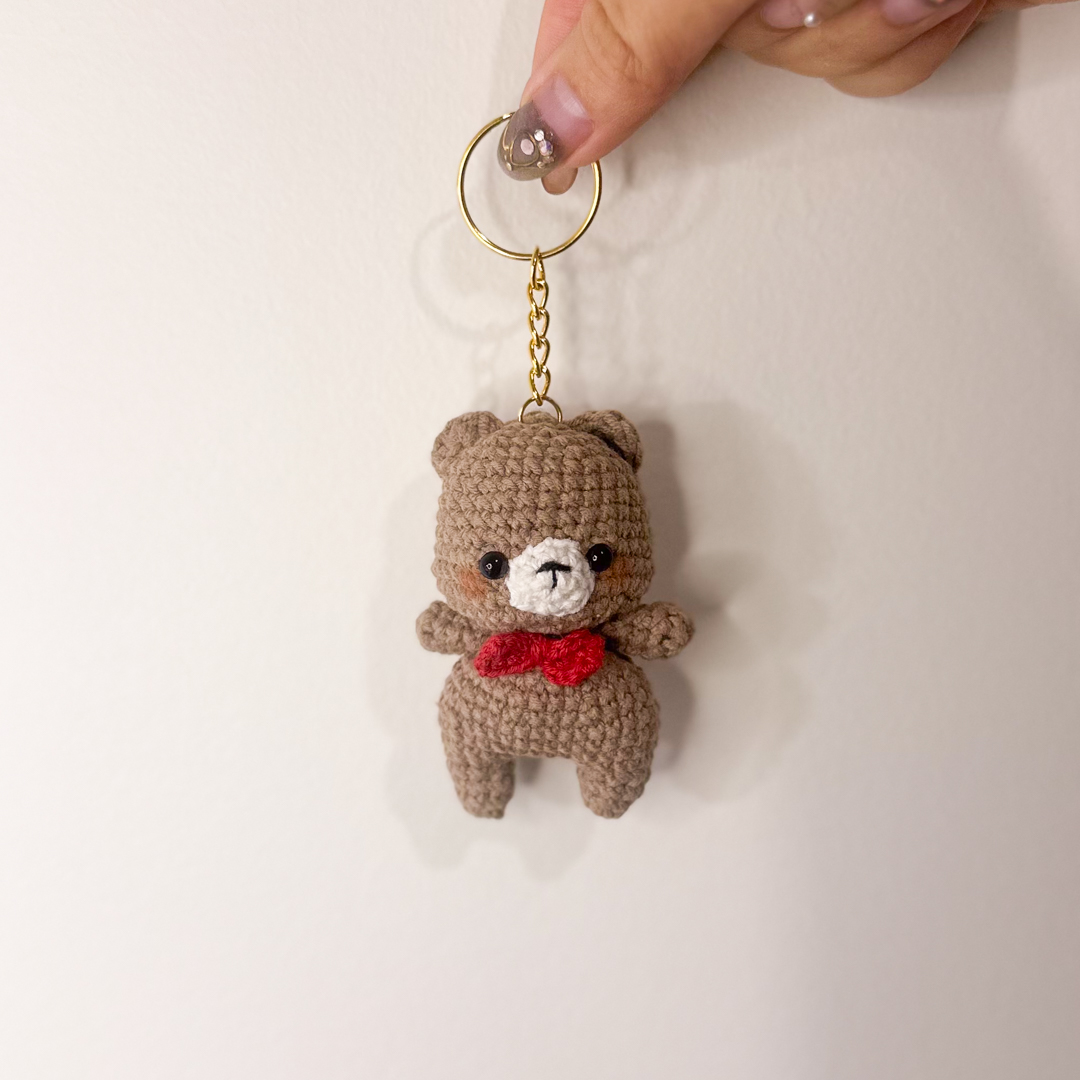 Brown bear keychain with a red bow, held in hand