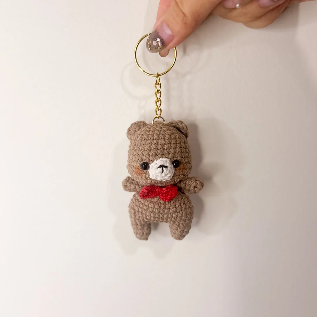 Brown bear keychain with a red bow, held in hand